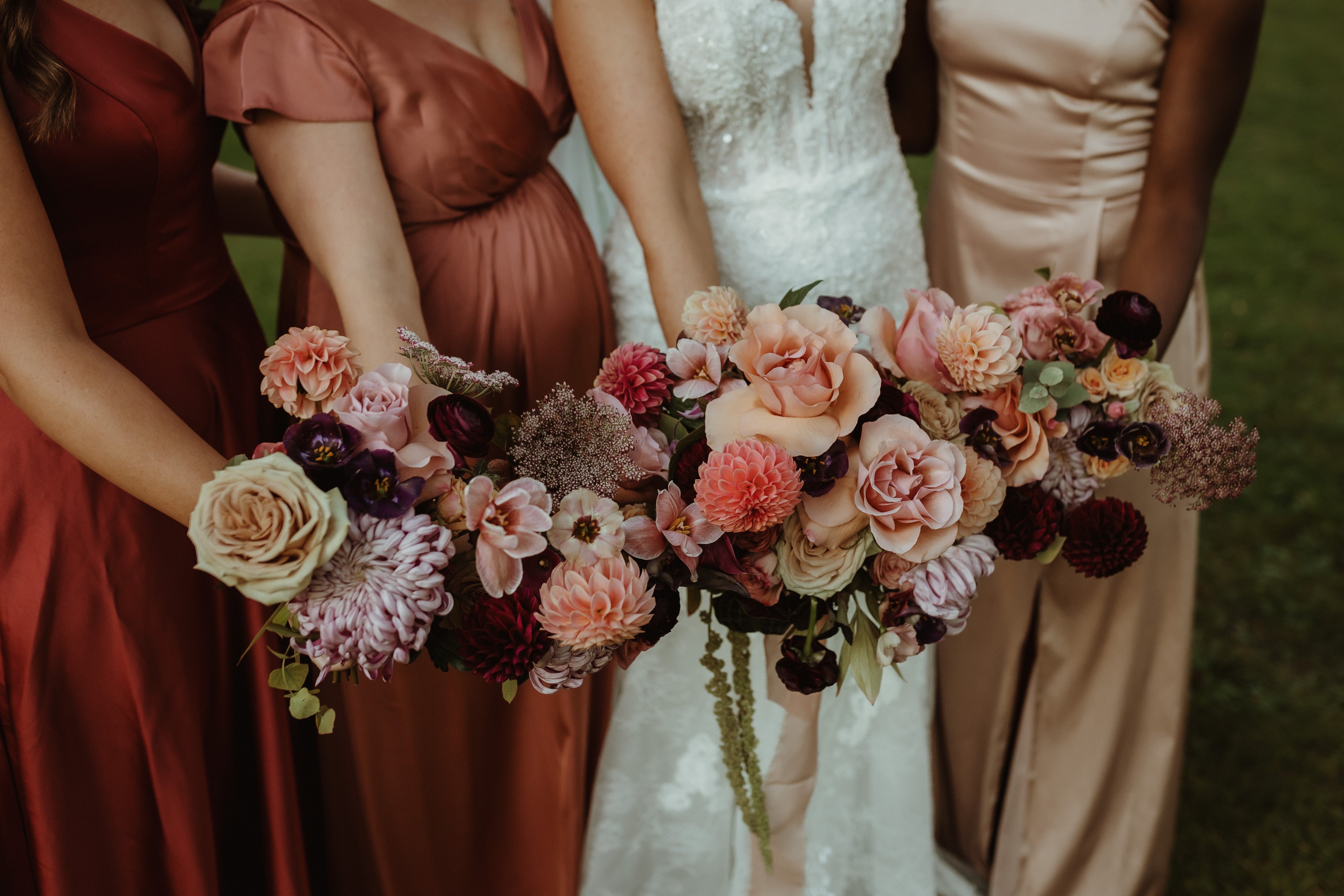 Bridesmaids in red and brown dresses holding floral bouquets with a bride in a white dress.