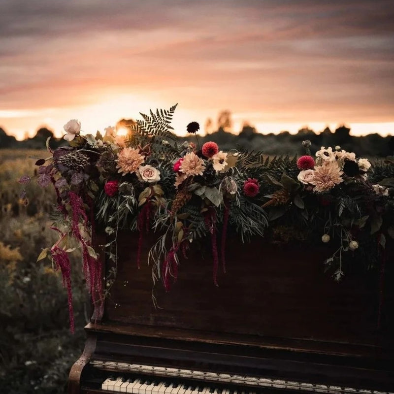 Floral arrangement on a piano in a field with a sunset sky